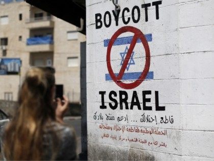 A tourist photographs a sign painted on a wall in the West Bank biblical town of Bethlehem on June 5, 2015, calling to boycott Israeli products coming from Jewish settlements. The international BDS (boycott, divestment and sanctions) campaign, that pushes for a ban on Israeli products, aims to exert political …
