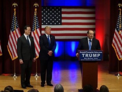 Donald Trump (C) looks on with Rick Santorm (L) as Mike Huckabee speaks during a Trump cam