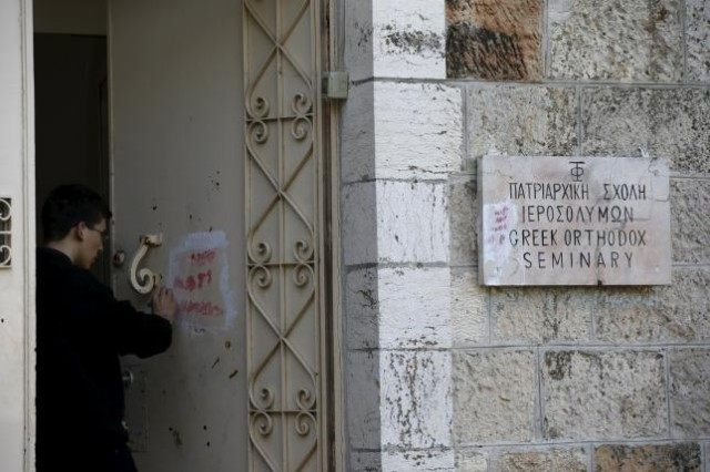 An Orthodox monk cleans graffiti from a door of the Greek Orthodox Seminary, located next