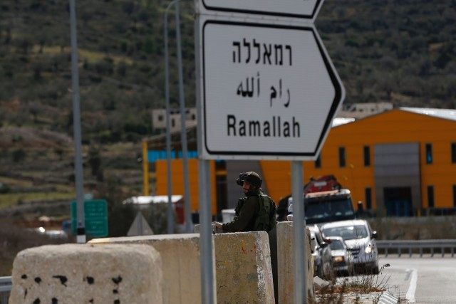 An Israeli soldier stands guard as he checks Palestinians' vehicles on their way out