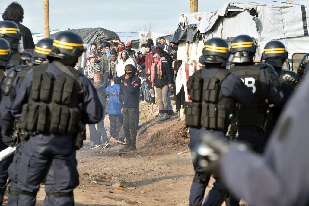 Anti-riot policemen face migrants on February 29, 2016, during the dismantling of half of the "Jungle" migrant camp in the French northern port city of Calais. Two bulldozers and around 20 workers began destroying makeshift shacks, with 30 police cars and two anti-riot vans stationed nearby. AFP PHOTO / PHILIPPE HUGUEN / AFP / PHILIPPE HUGUEN (Photo credit should read PHILIPPE HUGUEN/AFP/Getty Images)