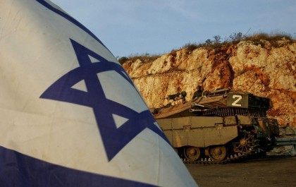 An Israeli soldier sits on a tank at a temporary military staging area along the Israel-Le