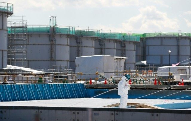 A worker wearing a protective suit and mask takes notes in front of storage tanks for radi