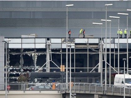 Workers walk on the roof of the damaged facade of Brussels airport in Zaventem on March 23