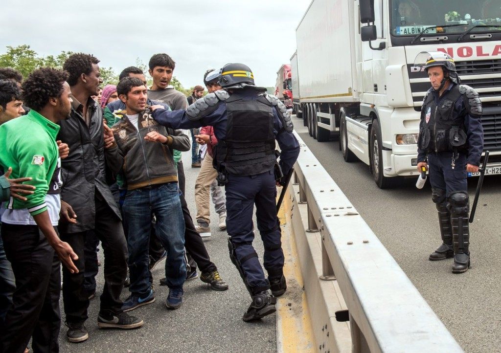 A French riot police officer (CRS) pushes back a man as illegal migrants wait to attempt to hide in lorries heading for England, in the French northern harbour of Calais, on June 17, 2015. AFP PHOTO / PHILIPPE HUGUEN (Photo credit should read PHILIPPE HUGUEN/AFP/Getty Images)