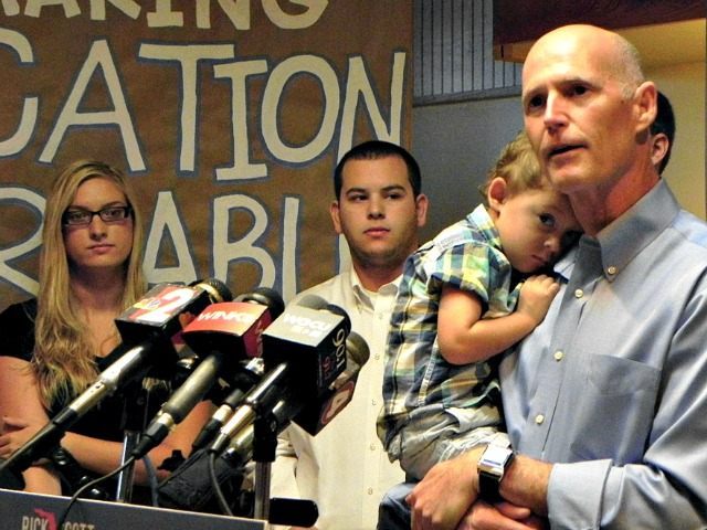 Gov. Rick Scott addresses media and supporters on Monday at Beef O’Brady’s in Estero, Fla.,where he discussed college affordability while holding his 2-year-old grandson, August. Scott wants to hold the line on tuition increases so more Floridians can earn degrees and enter the workforce with enhanced credentials. (AP Photo/The News-Press, …