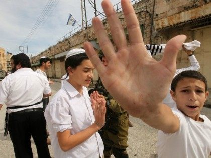 Israeli settler youth gesture to the camera in an attempt to block the view as security forces gather at the site where a Palestinian woman tried to stab an Israeli soldier before being shot dead, in the Israeli occupied West Bank city of Hebron, on February 13, 2016.