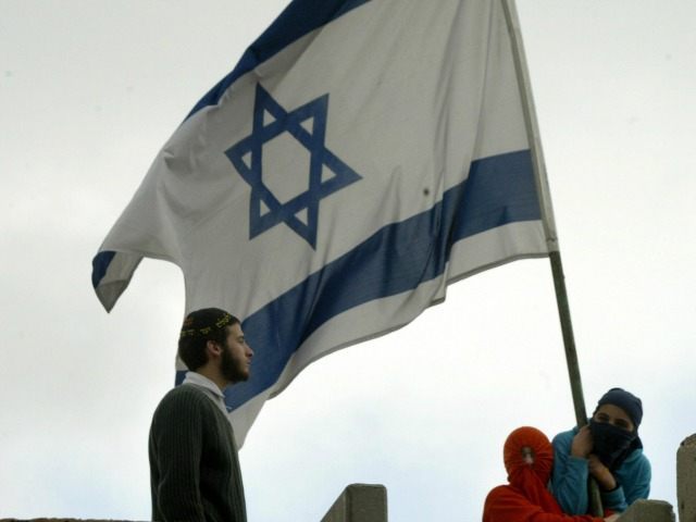 Jewish settlers, their faces covered, hold up an Israeli flag on the roof of a building in
