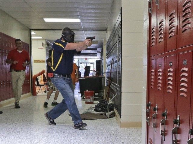 In this photo taken July 11, 2013, a Clarksville schools faculty member, wearing a protective mask, rear center, carries a practice handgun toward a classroom in the city's high school in Clarksville, Ark., as students portray victims in a mock school shooting scenario. Twenty Clarksville School District staff members are …