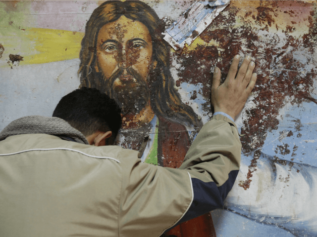 An Egyptian Christian mourns as he stands next to a blood-stained painting of Jesus Christ
