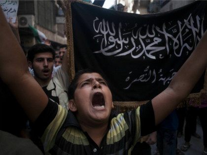 FILE - In this Sept. 21, 2012 file photo, a Syrian boy shouts slogans against the government as he stands in front of a flag of the armed Islamic opposition group, the Nusra Front, during a demonstration in the Bustan al-Qasr neighborhood of Aleppo, Syria. The country has already been …