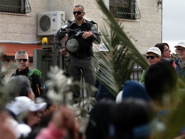 An Israeli policeman stands guarding the street as Christian worshippers attend a processi