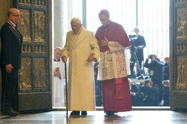 Pope Emeritus Benedict XVI (L) is helped by the prefect of the papal household Georg Gaens