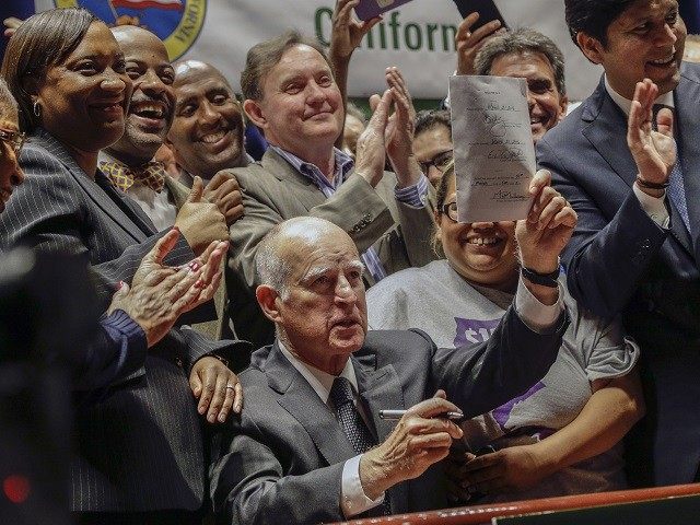 California Gov. Jerry Brown lifts a signed bill creating highest statewide minimum wage at $15 an hour by 2022 at the Ronald Reagan building in Los Angeles, Monday, April 4, 2016. California and New York acted Monday to gradually push their statewide minimum wages to $15 an hour, the highest …
