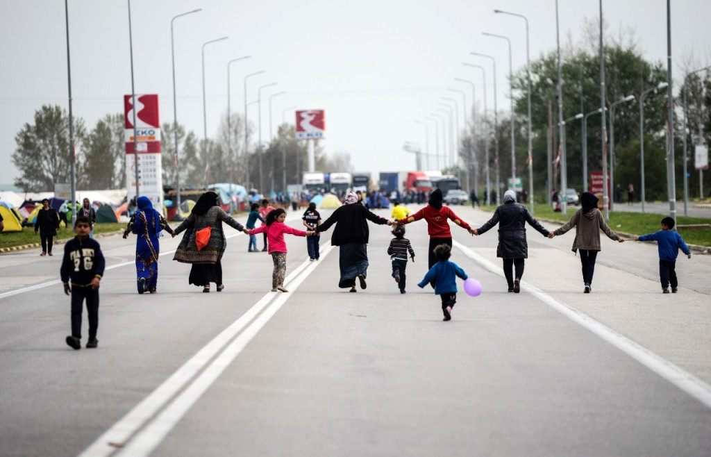 Migrants and refugees hold hands as they block the highway near the town of Polykastro to protest for the opening of the Greek-Macedonian border on April 2, 2016 after thousands of them are stranded by the Balkan border blockade. Migrant returns from Greece to Turkey will begin on April 4, 2016 under the terms of an EU deal that has worried aid groups, as Athens struggles to manage the overload of desperate people on its soil. Over 51,000 refugees and migrants seeking to reach northern Europe are stuck in Greece, after Balkan states sealed their borders. Hundreds more continue to land on the Greek islands every day despite the EU deal. / AFP / BULENT KILIC (Photo credit should read BULENT KILIC/AFP/Getty Images)