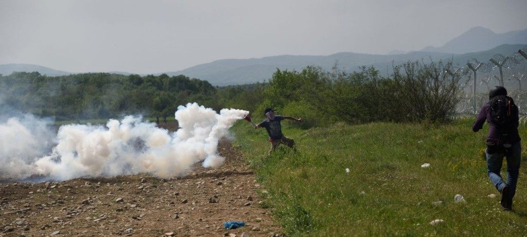 A man throws back to macedonian police a tear gas shell as migrants and refugees try to break down the border fence near their makeshift camp at the Greek-Macedonian border in Idomeni, on April 13, 2016. About 100 migrants spread out over about 100 metres (yards) tugging at the wire fence, but swiftly pulled back when two squads of Greek riot police moved in, the reporter said. The Greek riot police positioned themselves between the migrants and the Macedonian fence, ending the incident. / AFP / DANIEL MIHAILESCU (Photo credit should read DANIEL MIHAILESCU/AFP/Getty Images)