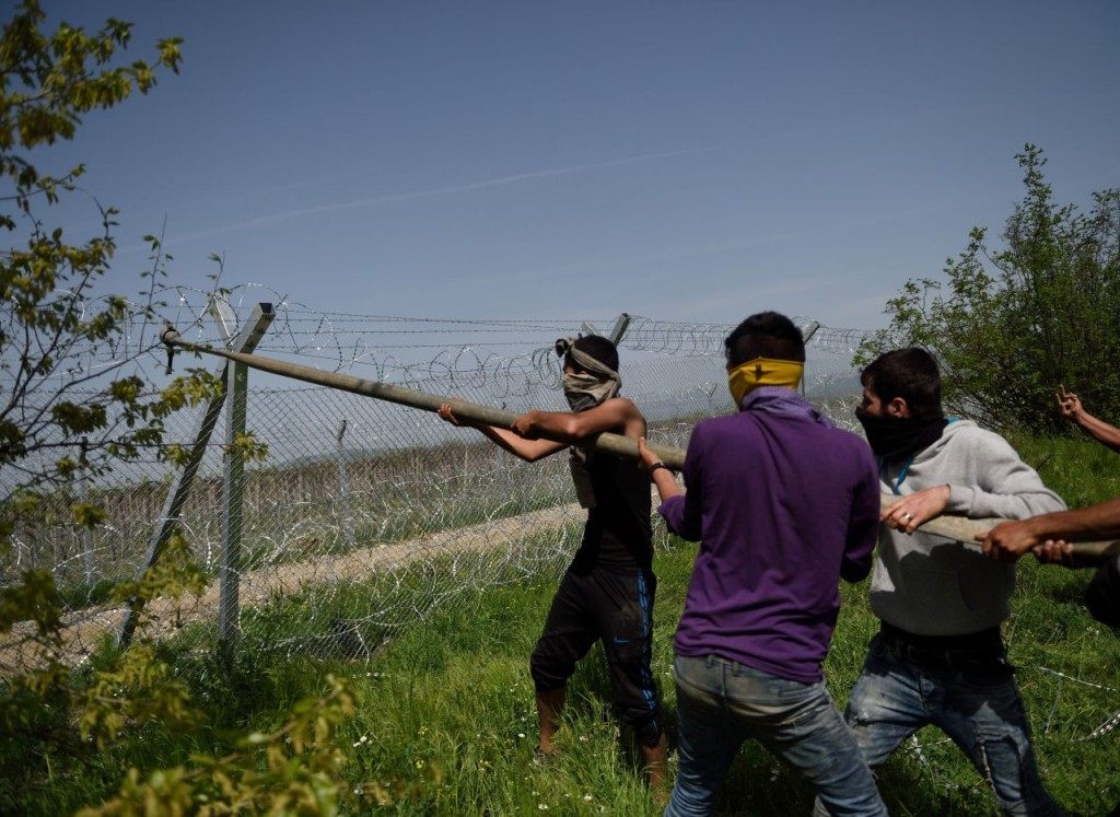 Men wearing scarves over their mouths use a pole to try and bring down the border fence between Greece and Macedonia near the Greek village of Idomeni on April 13, 2016. Macedonia police on April 13 fired tear gas and stun grenades at migrants staging a protest at the country's border fence with Greece, an AFP reporter said. About 100 migrants spread out over about 100 metres (yards) tugging at the wire fence, but swiftly pulled back when two squads of Greek riot police moved in, the reporter said. / AFP / DANIEL MIHAILESCU (Photo credit should read DANIEL MIHAILESCU/AFP/Getty Images)