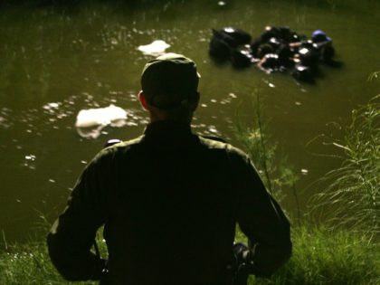 A US Border Patrol agent watches as a group of people use inner tubes to float down the New River, reportedly the most polluted river in the US, after illegally crossing the US/Mexico border on March 27, 2005 near Calexico, California. The black plastic bags are for carrying a dry …