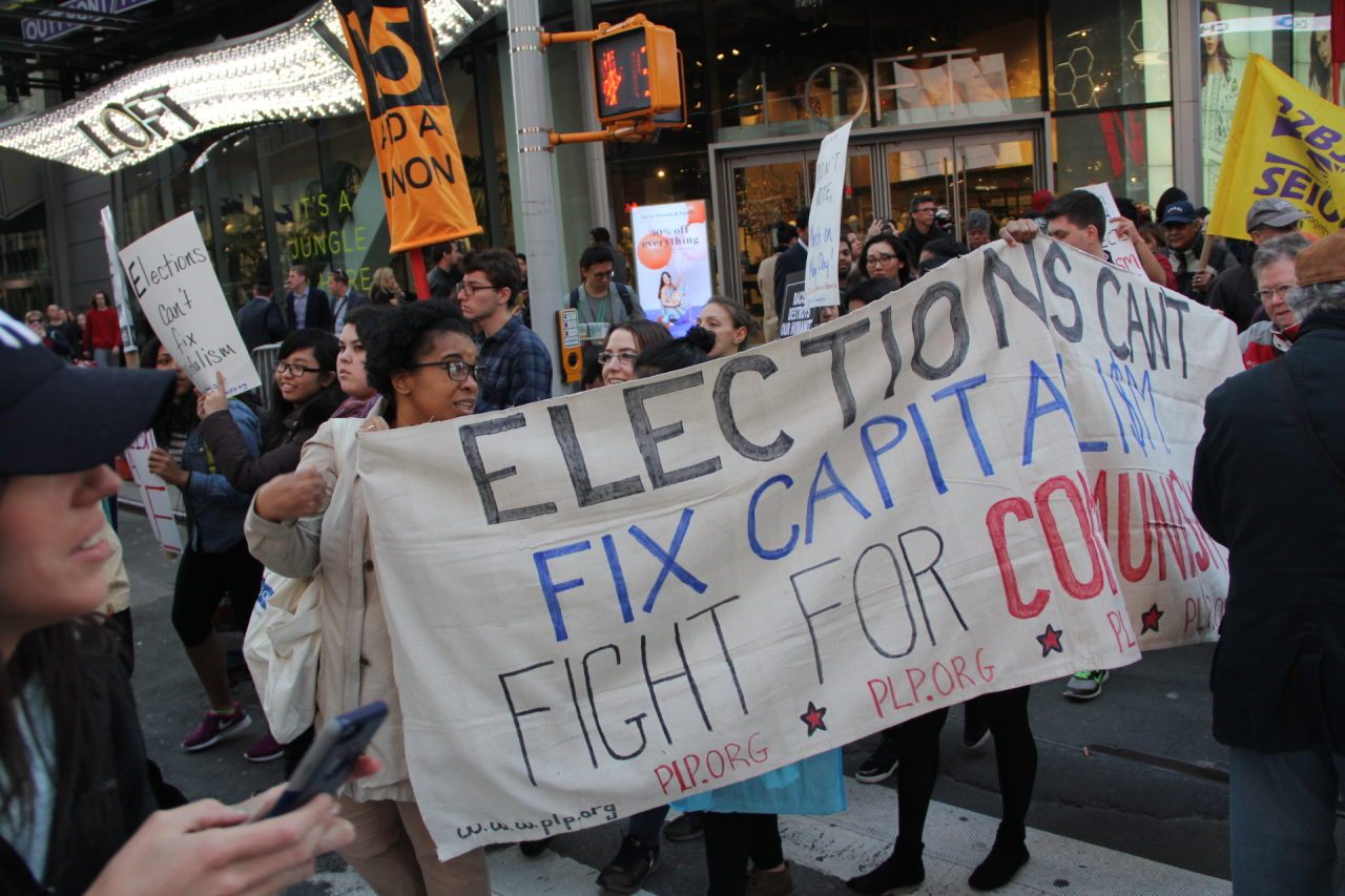Protesters carry a sign: "Elections won't fix capitalism"