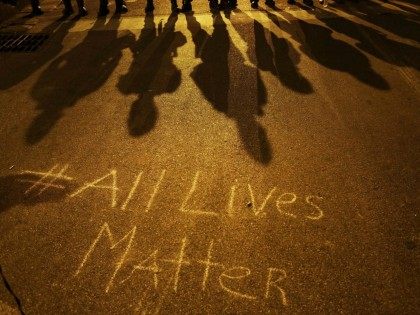 A message reading "All Lives Matter" is written on the pavement as police in riot gear cast shadows while standing in line ahead of a curfew Friday, May 1, 2015, in Baltimore. (AP Photo/David Goldman)