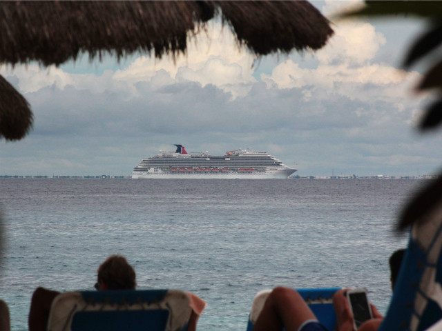 Tourists lie on the beach as cruise ship Carnival Magic is seen near the shores of Cozumel