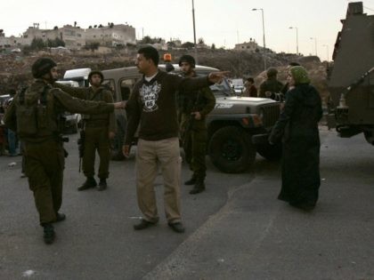 Israeli soldiers speak to a Palestinian man as he waits to cross the Kalandia checkpoint o