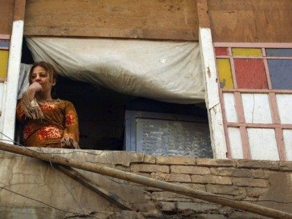 An Iraqi woman watches US Army soldiers from a balcony looking over a Baghdad street 22 May 2003. The US army was summoned by prostitutes living in the building after a firefight between prostitutes and gang members erupted over stolen merchandise.
