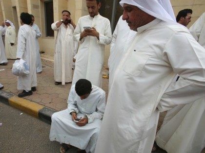 Kuwaiti men use smartphones as they gather outside the Shiite Al-Imam al-Sadeq mosque foll