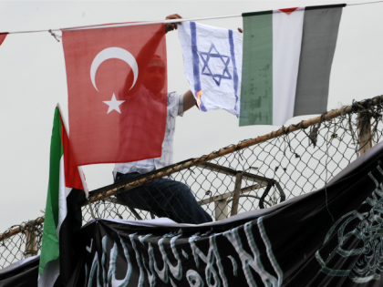 A demonstrator burns an Israeli flag as he sits between Turkish (L) and Palestinian flags