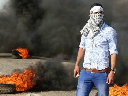 A Palestinian protester stands amid burning tires during clashes with Israeli security for