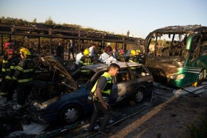 Israeli firemen and emergency services gather around the remains of a burnt-out a bus and