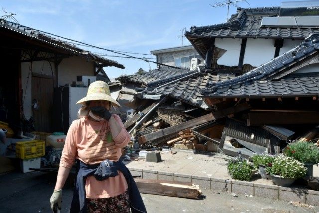 A woman stands in front of her damaged house in Mashiki, Kumamoto prefecture on April 15,