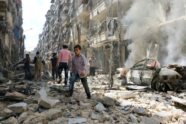 People walk amid the rubble of destroyed buildings following an air strike on the rebel-he