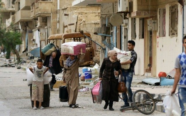 Syrians carry their belongings upon their return to the modern town of Palmyra, adjacent t