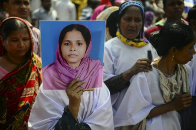 A woman holds a picture of a relative who died in the Rana Plaza building collapse, as peo