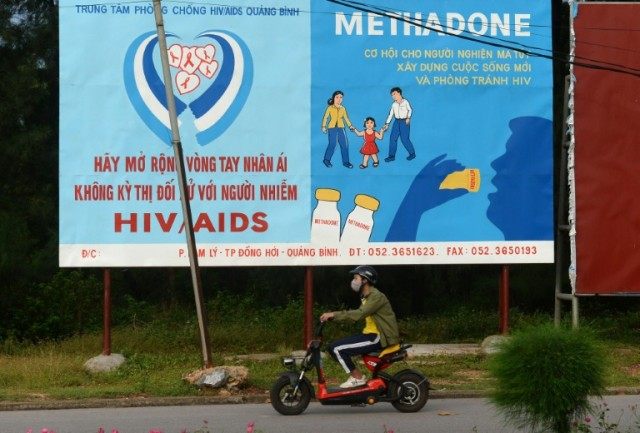 A motorcyclist in Dong Hoi City, Vietnam, rides past a poster advising drug addicts to use