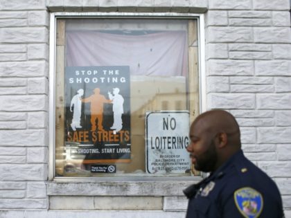 In this March 31, 2016 photo, Baltimore Police Department Officer Jordan Distance walks past signs in a row home's window during a foot patrol in Baltimore. In the year since Freddie Gray died, the Baltimore police department has worked on its relationship with the community and tried to heal wounds …