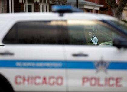 CHICAGO, IL - APRIL 25: A Chicago Police officer is seen through a police vehicle window as he stands at the crime scene where a 16-year-old boy was shot in the head and killed and another 18-year-old man was shot and wounded on the 7300 block of South Sangamon Street …