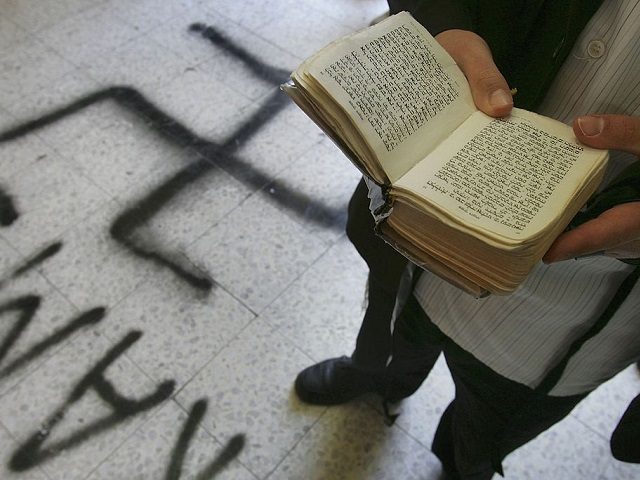 PETAH TIKVA, ISRAEL - MAY 4: A religious Jew recites prayers over a Swastika that desecrates the floor of the Grand Synagogue May 4, 2006 in Petah Tikva in central Israel. Jewish worshippers arriving for early morning prayers found the synagogue desecrated with Swastika and crucifix graffiti on its floors, …