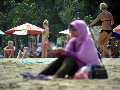 A Muslim woman wearing a veil sits in front of foreign tourists wearing bikinis on Kuta be