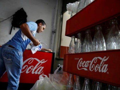 Cases of Coca-Cola with empty bottles are seen next to a man cleaning a fridge with the lo