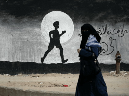 A Palestinian woman walks past a graffiti painted on a wall of the United Nations school of Beit Hanun, in the northern Gaza Strip, on May 9, 2016.