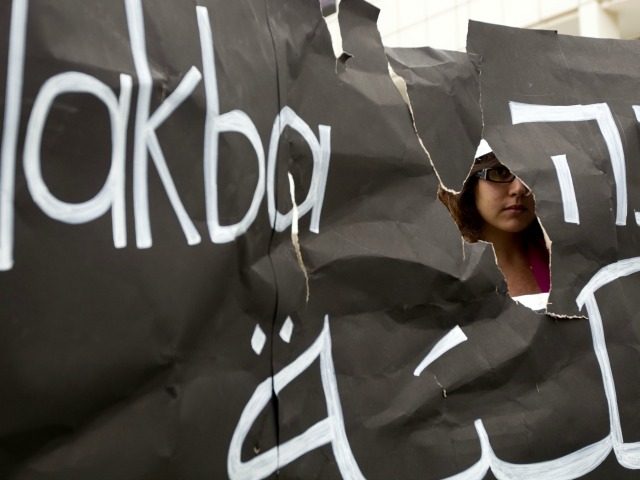 An Israeli Arab student is seen through a torn placard during a ceremony commemorating the