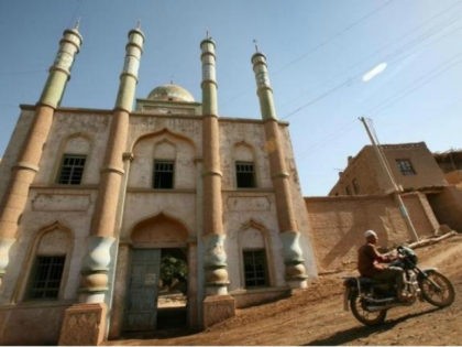 A man rides his motorcycle in front of a mosque at a village near the city of Turpan in Ch