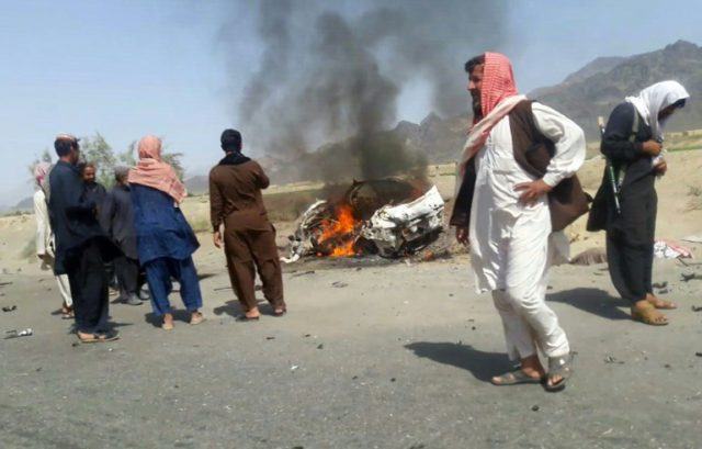 Pakistani local residents gathering around a destroyed vehicle hit by a drone strike in wh