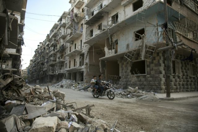 Syrian men ride a motorbike past damaged buildings in the rebel-held Bustan al-Qasr distri