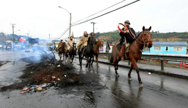 Local residents riding horses pass along a burnt out barricade in a street of Castro, Chil