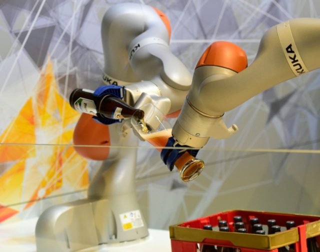 Two robots fill a glass with beer at the booth of robotics manufacturer KUKA at a fair in
