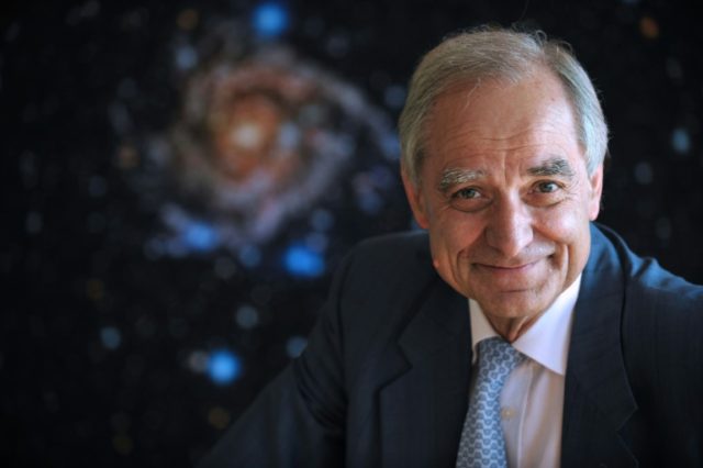 French astrophysician Andre Brahic poses in front of a picture of the IC 342 galaxy at the