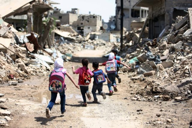 Syrian schoolchildren run past damaged buildings in the rebel-held are of Jobar, on the ea